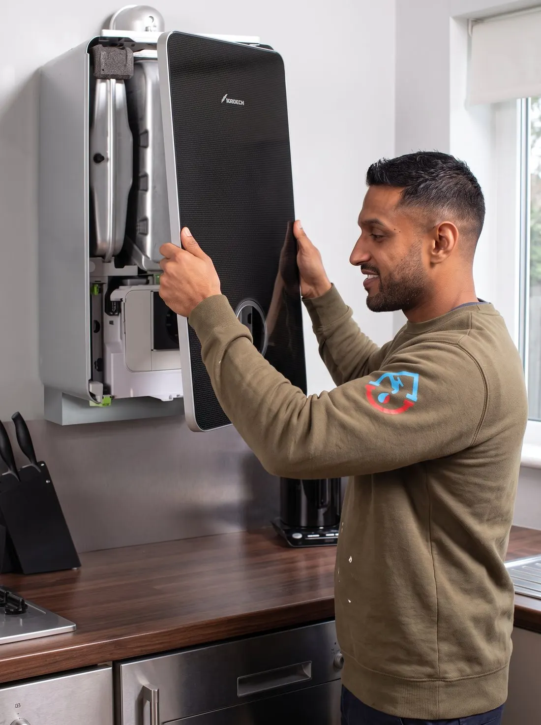 Engineer fitting the front panel to a wall-hung combi boiler in a kitchen